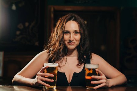 Foto de Sexy mujer con grandes pechos con dos vasos de cerveza lager en la mano en el bar en el pub - Imagen libre de derechos