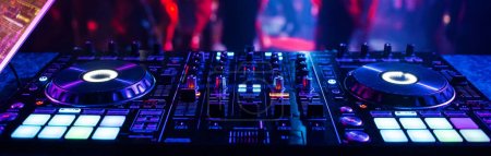 mezclador de DJ controlador de música en un club nocturno en una fiesta en el fondo de siluetas borrosas de personas bailando
