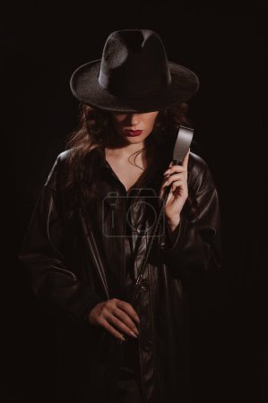 Foto de Mujer en un impermeable de cuero y sombrero con un látigo flogger para el sexo BDSM con sumisión y dominación - Imagen libre de derechos