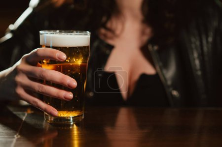 Photo pour Femme avec de gros seins tient un verre de bière lager avec de la mousse dans sa main au bar - image libre de droit