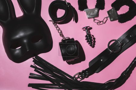 Téléchargez les photos : Set of adult erotic toys for BDSM sex with submission and domination. Leather flogger whip, handcuffs, mask on pink background - en image libre de droit
