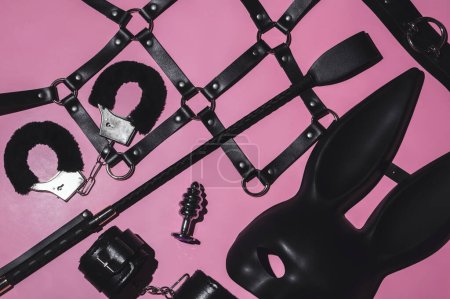 Foto de Set of adult erotic toys for BDSM sex with submission and domination. Leather flogger whip, handcuffs, mask on pink background - Imagen libre de derechos