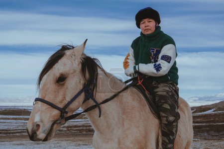 Téléchargez les photos : TAU SAMALY, KAZAKHSTAN - 23 DÉCEMBRE 2023 : Kazakhe chevauchant un cheval en hiver dans un champ près de Tau Samaly au Kazakhstan - en image libre de droit
