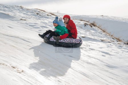 Foto de TAU SAMALY, KAZAKHSTAN - 23 de diciembre de 2023: feliz familia kazaja recorriendo un tobogán en invierno con nieve en el centro recreativo Tau Samaly en Kazajstán - Imagen libre de derechos