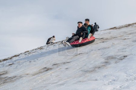 Téléchargez les photos : TAU SAMALY, KAZAKHSTAN - 23 DÉCEMBRE 2023 : des amis kazakhs heureux descendent un toboggan en hiver avec de la neige au centre récréatif Tau Samaly au Kazakhstan - en image libre de droit