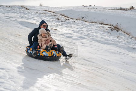 Téléchargez les photos : TAU SAMALY, KAZAKHSTAN - 23 DÉCEMBRE 2023 : heureux Kazakhs un père homme avec une fille enfant descendant un toboggan en hiver avec de la neige au centre récréatif Tau Samaly au Kazakhstan - en image libre de droit