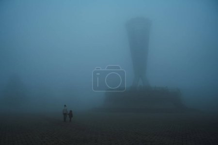 Téléchargez les photos : Dos de mère femme avec enfant fils marchant dans un parc mystique brumeux en soirée. Un paysage brumeux avec des gens en automne dans une brume de brouillard brumeux dans le parc de l'indépendance à Shymkent au Kazakhstan - en image libre de droit