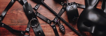Téléchargez les photos : Set of BDSM sex toys with handcuffs, whip flogger, butt anal plug for submission and domination on wooden background. Wide header cover for a horizontal banner for sex shop - en image libre de droit