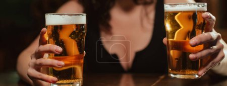 Foto de Dos vasos de cerveza de espuma ligera lager en las manos de una mujer con grandes senos sexy en el bar en el pub - Imagen libre de derechos