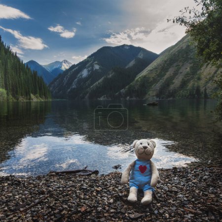 toy plush teddy bear sits relax on rocks near Kolsay Lake in Kazakhstan in the Tien Shan Mountains in summer