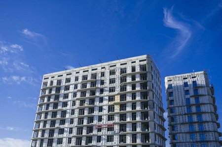 Foto de SHYMKENT, KAZAKHSAN - ENERO 03, 2024: edificio residencial en construcción con paneles de aislamiento térmico instalados en la fachada sobre un fondo azul del cielo - Imagen libre de derechos