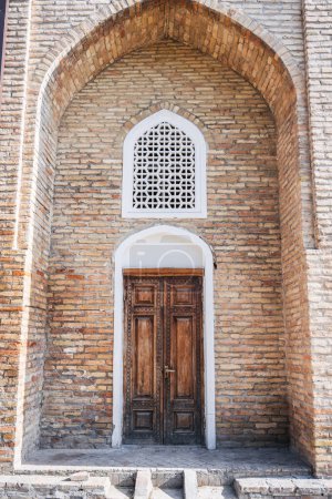 Téléchargez les photos : Ancienne porte en bois sculpté avec motif oriental ouzbek en mur de briques avec arche dans la Madrasah Barak-Khan à Tachkent en Ouzbékistan - en image libre de droit