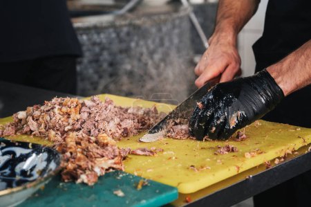 männlicher Koch schneidet gekochtes Rindfleisch mit einem Messer auf einem Schneidebrett zum Kochen usbekischer Pilaf in der Küche eines Restaurants in Taschkent in Usbekistan