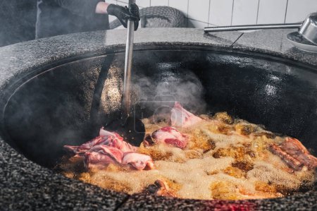 männlicher Koch kocht Lammfleisch in einem siedenden Kessel für traditionelle orientalische usbekische Pilaf in der Küche in Usbekistan in Taschkent