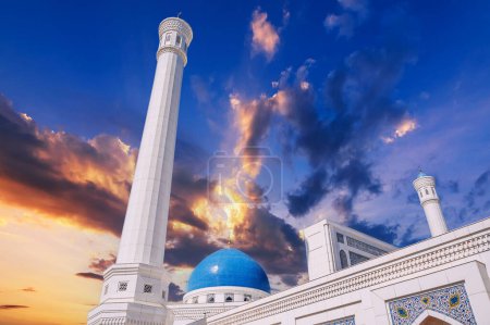 high white minaret and blue dome of modern Islamic Masjid Minor Mosque in Tashkent in Uzbekistan on background of the sunset sky