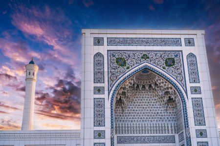 white marble wall decorated uzbek ornaments and minaret of the modern Islamic Masjid Minor Mosque in Tashkent in Uzbekistan on background of sunset sky