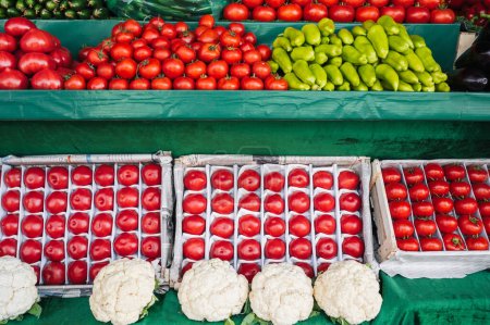 counter with fresh vegetables at a grocery farmers market. Tomatoes, cucumbers, cauliflower and peppers on store shelves