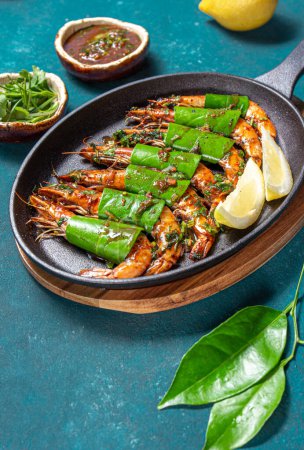 Photo for Spicy garlic tiger Prawns Shrimps on frying pan with lemon leaves on blue bakground, close up. - Royalty Free Image