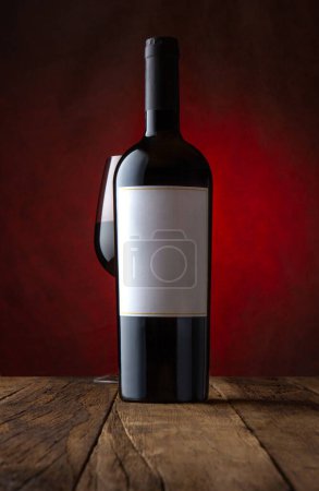 Foto de Foto promocional de copa y botella de vino tinto con etiqueta vacía de fondo marrón oxidado. Burla, vista frontal. - Imagen libre de derechos