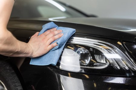Jeune homme nettoyage à la main de la lampe frontale d'une voiture moderne dans le studio de détail, détail du concept de voiture