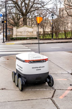 Foto de Un robot de reparto de comida de Starship está conduciendo en la acera en el campus de la Universidad de Pittsburgh en Pittsburgh, PA, EE.UU. el 11 de enero de 2020. Los Robots están entregando comida de cuatro restaurantes del campus. - Imagen libre de derechos