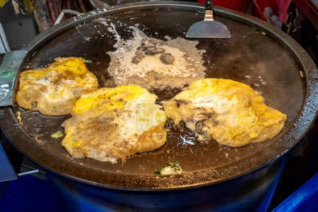 Comida callejera taiwanesa: tortilla de ostras en el plato caliente de un vendedor de comida callejera en el mercado nocturno de Taipei, Taiwán