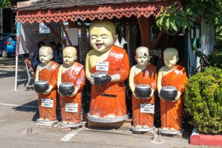 Téléchargez les photos : Statues de quatre moines débutants bouddhistes souriants tenant des récipients d'aumônes avec des signes de boîte de don - en image libre de droit