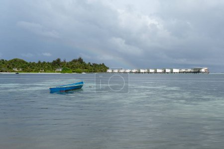 Téléchargez les photos : Un bateau bleu sur l'eau aux Maldives avec des villas insulaires et aquatiques en arrière-plan - en image libre de droit