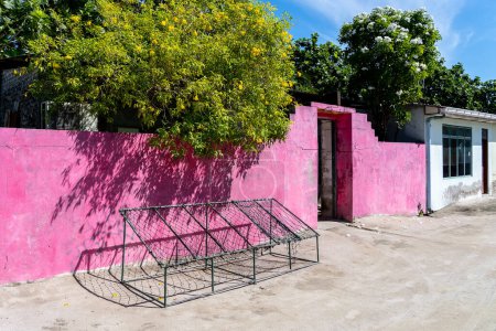 Traditionelle Outdoor-Seilstühle vor einer rosafarbenen Wand auf der Straße einer lokalen Wohninsel auf den Malediven.