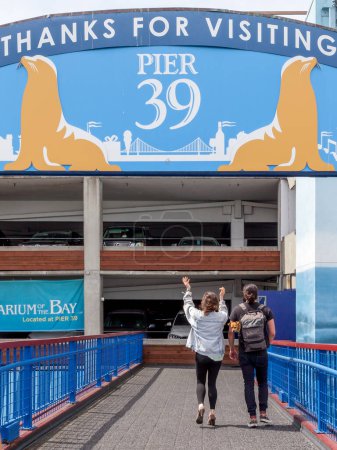 Photo for San Francisco, California, USA - April 2, 2018: Two people with a small dog walking to Pier 39 parking garage. Pier 39 is a shopping center and popular tourist attraction built on a pier. - Royalty Free Image