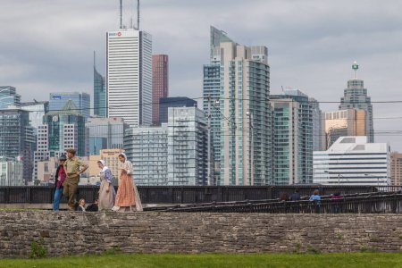 Téléchargez les photos : TORONTO, ONT, CANADA- LE 27 MAI 2017 : Des membres du personnel déguisés au lieu historique national du Fort-York avec la ville en arrière-plan. La plus importante collection de sites de bataille de la guerre de 1812 et de 1813 au Canada. - en image libre de droit
