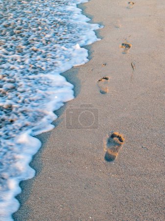 Téléchargez les photos : Vagues de mousse de mer lavant les empreintes sur le sable de la plage le matin. - en image libre de droit