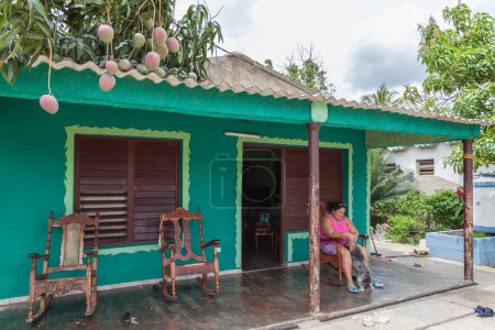 Foto de GUAMA, CUBA - 19 DE ABRIL DE 2017: Mujer cubana sentada en el porche de su casa jugando con su perro en el pueblo de Guama, Cuba - Imagen libre de derechos