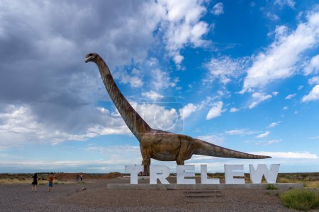 Téléchargez les photos : Province de Chubut, Argentine - 20 janvier 2023 : Visiteurs observant la réplique de Titanosaurus avec panneau Trelew près du Museo Paleontologico Egidio Feruglio (MEF) à Trelew, province de Chubut, Argentine. - en image libre de droit