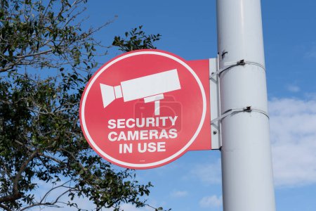 Téléchargez les photos : Un rouge Caméras de sécurité en cours d'utilisation signe sur le poteau lumineux avec un arbre et le ciel bleu en arrière-plan. - en image libre de droit