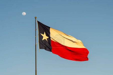 Foto de Bandera de Texas ondeando en el viento con cielo azul y luna en el fondo. Texas es un estado en la región Centro-Sur de los Estados Unidos.. - Imagen libre de derechos