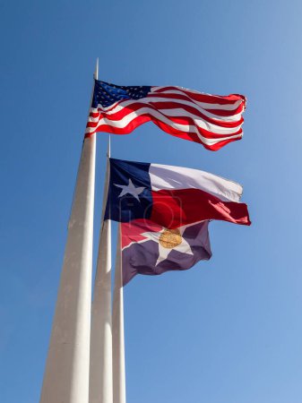 Bandera de los Estados Unidos, Bandera de Texas y Bandera de Dallas ondeando al viento con fondo azul en City Hall Plaza en Dallas, TX, EE.UU..