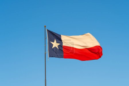 Foto de Bandera de Texas ondeando en el viento con el cielo azul de fondo. Texas es un estado en la región Centro-Sur de los Estados Unidos.. - Imagen libre de derechos