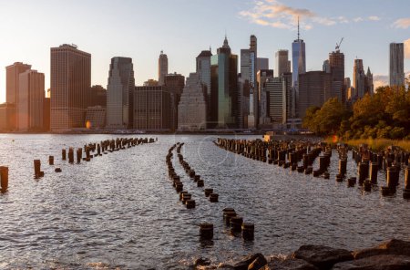 Téléchargez les photos : Superbe coucher de soleil et horizon du Lower Manhattan avec East River et New York City. Crépuscule avec réflexions et jetée abandonnée au coucher du soleil depuis Brooklyn Bridge Park - en image libre de droit
