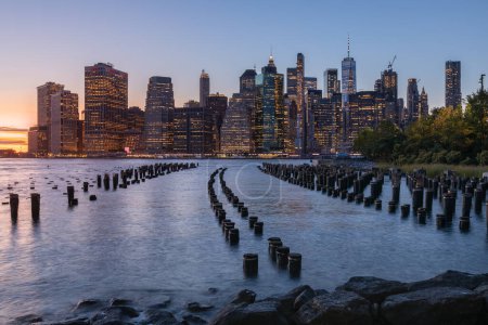 Téléchargez les photos : Beautiful Sunset and Lower Manhattan skyline with East River and New York City. Twilight with Reflections and Abandoned Pier at Sunset from Brooklyn Bridge Park - en image libre de droit