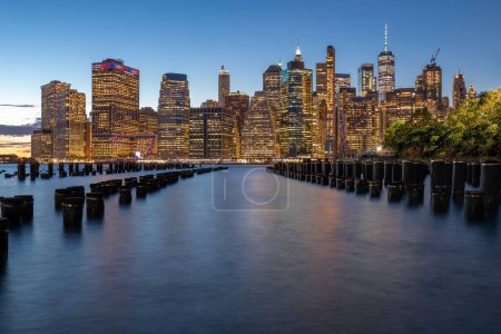 Téléchargez les photos : Beautiful Sunset and Lower Manhattan skyline with East River and New York City. Twilight with Reflections and Abandoned Pier at Sunset from Brooklyn Bridge Park - en image libre de droit