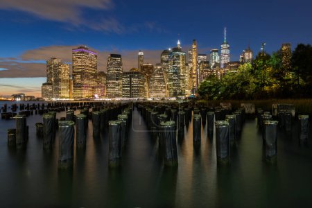 Foto de Hermosa luz nocturna y horizonte del Bajo Manhattan con East River y Nueva York. Crepúsculo con reflexiones y muelle abandonado al atardecer desde Brooklyn Bridge Park - Imagen libre de derechos