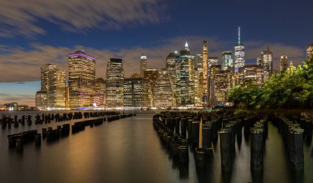 Téléchargez les photos : Belle veilleuse et horizon du Lower Manhattan avec East River et New York. Crépuscule avec réflexions et jetée abandonnée au coucher du soleil depuis Brooklyn Bridge Park - en image libre de droit