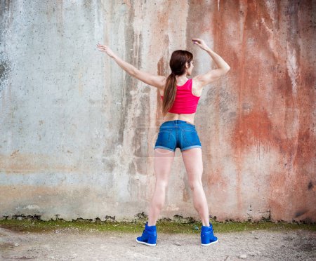 Foto de Hermosa mujer de fitness posando después de trabajar duro en un edificio abandonado. Camisa roja y Jeans. - Imagen libre de derechos