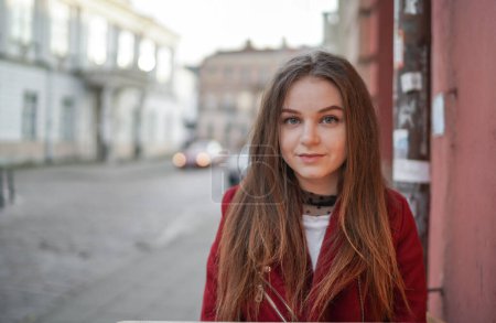 Téléchargez les photos : Gros plan Visage d'une belle jeune fille dans la vieille ville de Vilnius, Lituanie. Veste rouge et pantalon noir. Belle journée du printemps. Visage curieux - en image libre de droit