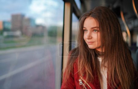 Téléchargez les photos : Belle jeune fille va dans le chariot dans la vieille ville de Vilnius, Lituanie. Elle porte une veste rouge. Belle heure du coucher du soleil au printemps. Souriant. - en image libre de droit
