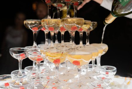 Foto de Champagne glasses standing in a tower at the wedding party. Champagne glass pyramid. Pyramid of glasses of wine, champagne, tower of champagne. Wedding party at night - Imagen libre de derechos