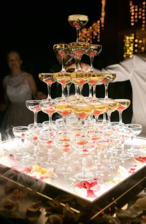 Foto de Champagne glasses standing in a tower at the wedding party. Champagne glass pyramid. Pyramid of glasses of wine, champagne, tower of champagne. Wedding party at night - Imagen libre de derechos