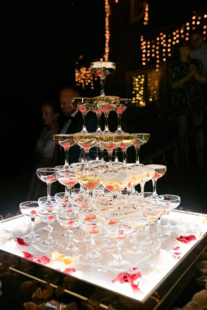 Photo for Champagne glasses standing in a tower at the wedding party. Champagne glass pyramid. Pyramid of glasses of wine, champagne, tower of champagne. Wedding party at night - Royalty Free Image