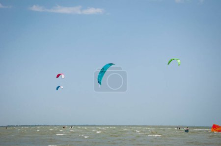 Photo for Henichesk, Ukraine - July 12, 2021: Kitesurfing. Seascape with kitesurfer in waves. Surfer in wetsuit doing trick in air against sea. Kitesurfing athlete on kite with board. - Royalty Free Image